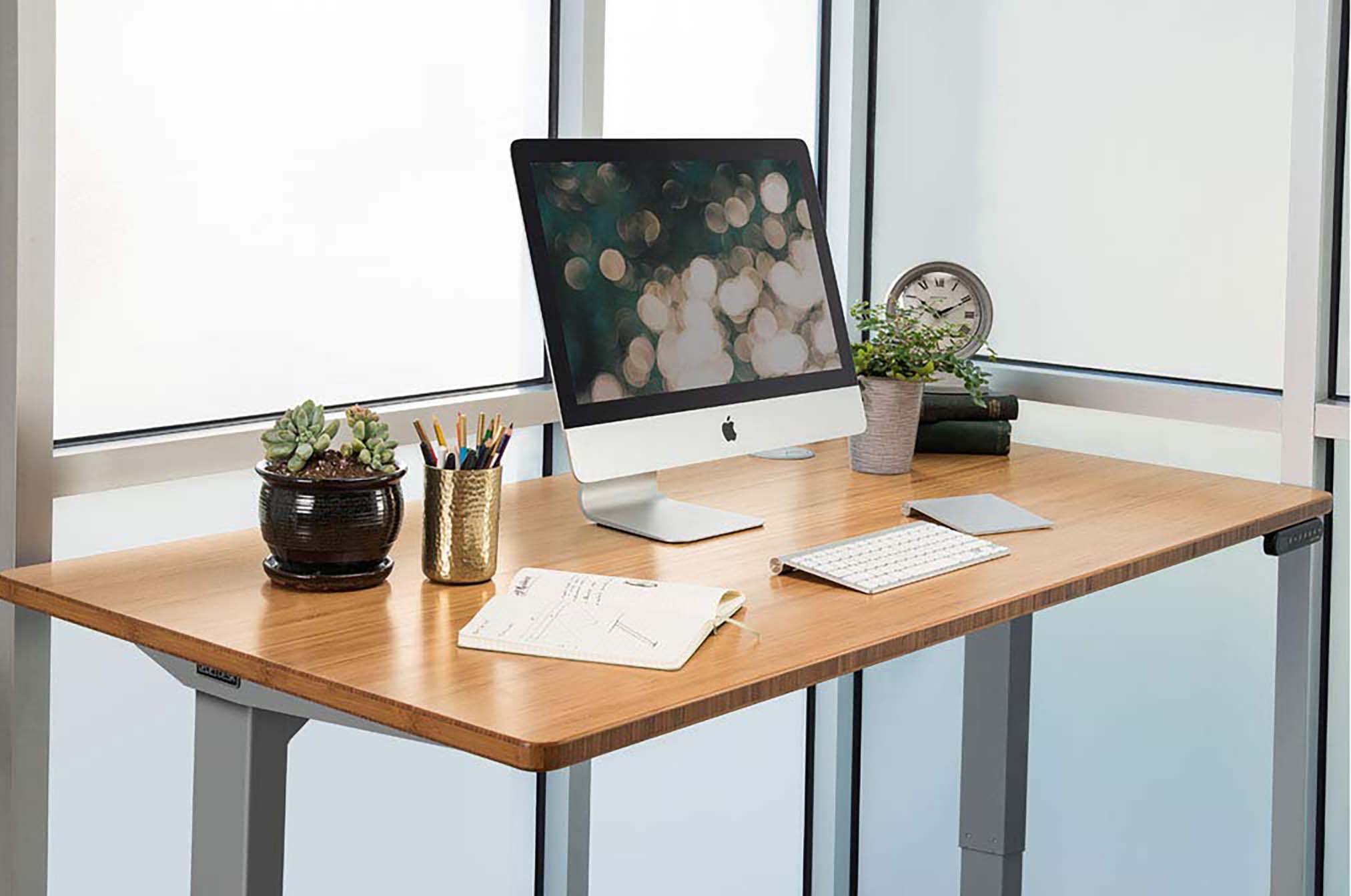 Stock UPLIFT V2 standing desk with an iMac on top and several office supplies and plants